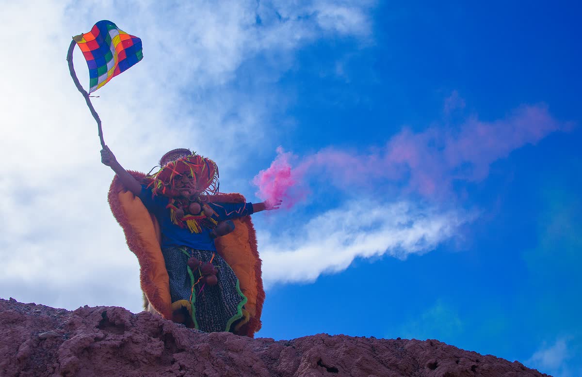 Un diablo de carnaval con su bandera en lo alto del cerro, entre humo de color