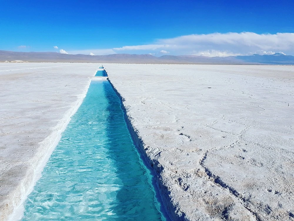 Pileta de agua turquesa abierta en la costra blanca de las Salinas Grandes